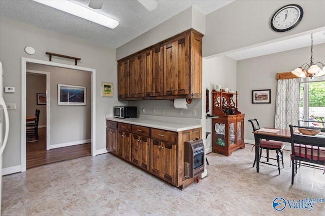 kitchen with decorative light fixtures, heating unit, light countertops, stainless steel microwave, and ceiling fan with notable chandelier