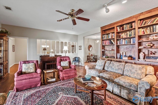 living room featuring ceiling fan with notable chandelier, a textured ceiling, and wood finished floors