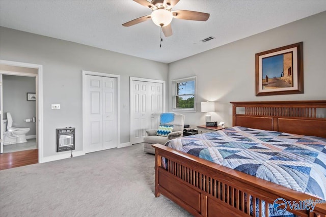 bedroom featuring light carpet, visible vents, heating unit, a textured ceiling, and multiple closets