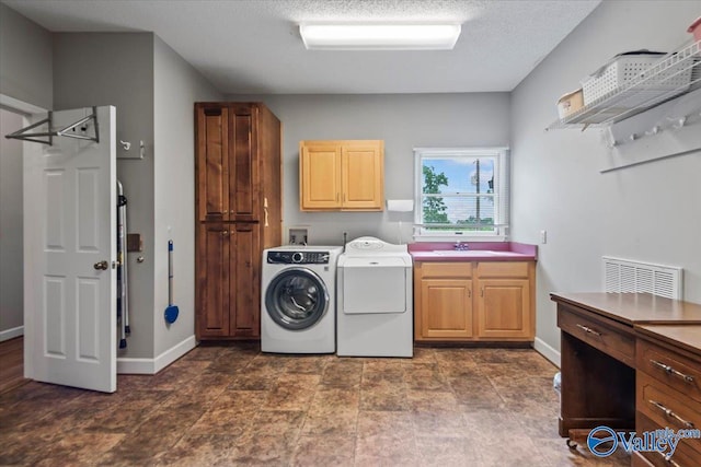 laundry area featuring cabinet space, baseboards, a textured ceiling, washer and dryer, and a sink