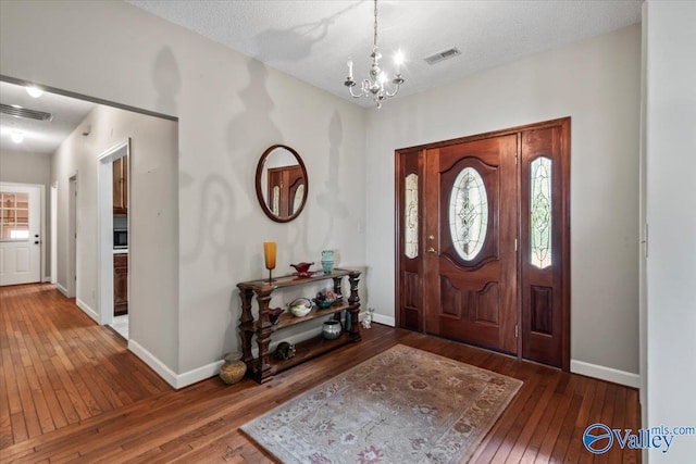 entrance foyer with visible vents, dark wood finished floors, baseboards, and an inviting chandelier