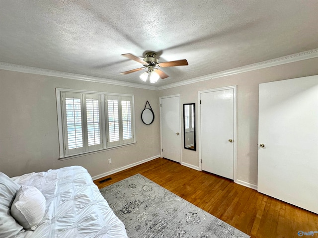 bedroom with a textured ceiling, dark wood-type flooring, ceiling fan, and crown molding