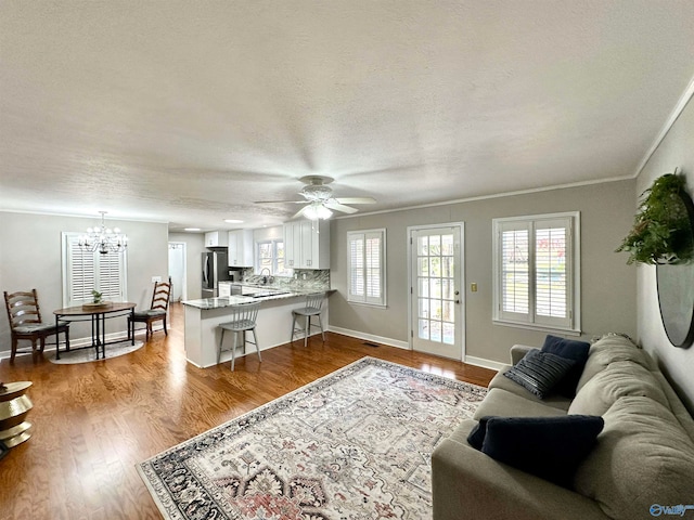 living room featuring ceiling fan with notable chandelier, light hardwood / wood-style floors, a textured ceiling, sink, and ornamental molding