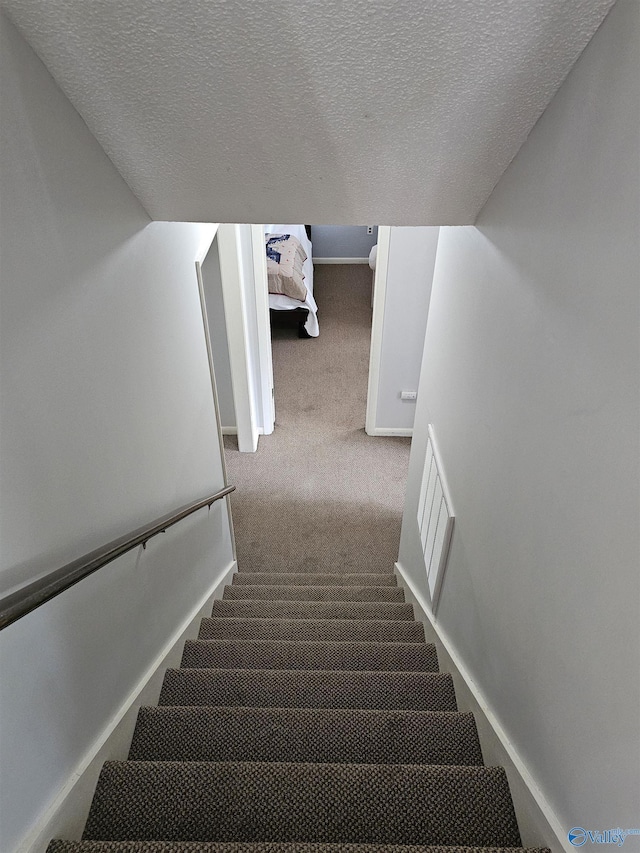 stairway featuring carpet floors and a textured ceiling