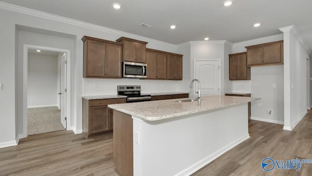 kitchen featuring appliances with stainless steel finishes, sink, a center island with sink, and light stone counters