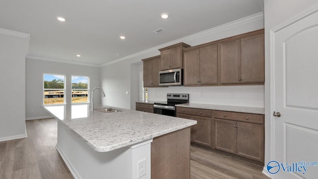 kitchen featuring appliances with stainless steel finishes, sink, a kitchen island with sink, crown molding, and light wood-type flooring
