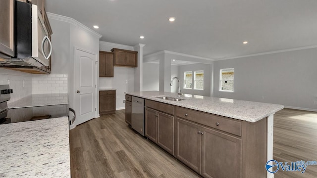kitchen featuring sink, tasteful backsplash, a center island with sink, stainless steel appliances, and light stone countertops