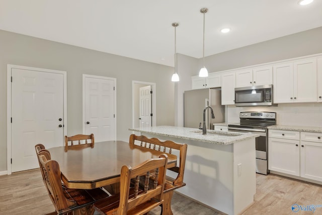 kitchen featuring decorative light fixtures, appliances with stainless steel finishes, white cabinetry, and light hardwood / wood-style floors