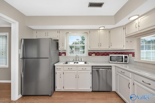 kitchen with stainless steel appliances, a wealth of natural light, sink, and light hardwood / wood-style flooring