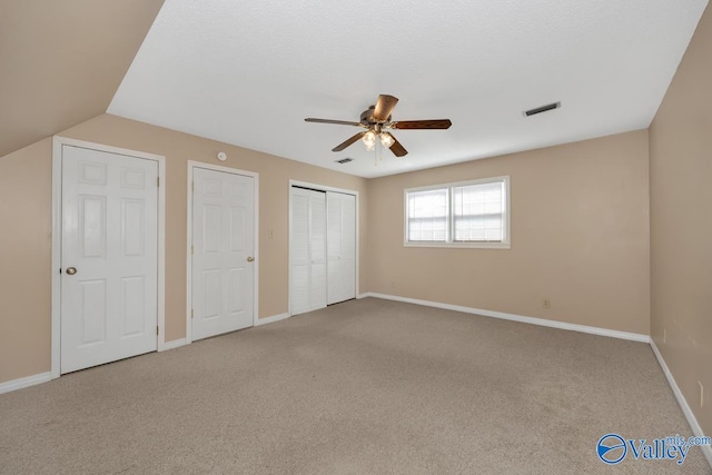 unfurnished bedroom with lofted ceiling, two closets, carpet, and ceiling fan