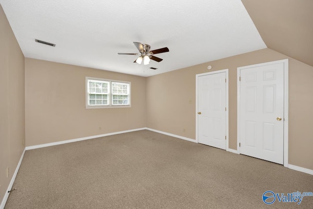 unfurnished bedroom featuring ceiling fan, a textured ceiling, vaulted ceiling, and carpet