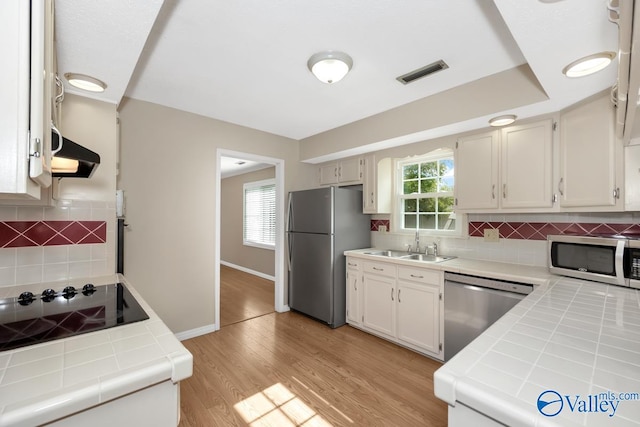 kitchen with tile counters, stainless steel appliances, a healthy amount of sunlight, and ventilation hood