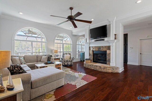 living room with a stone fireplace, dark hardwood / wood-style flooring, ornamental molding, and ceiling fan