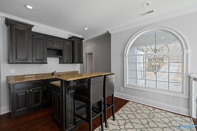 kitchen with dark hardwood / wood-style floors, light stone countertops, a center island, and ornamental molding