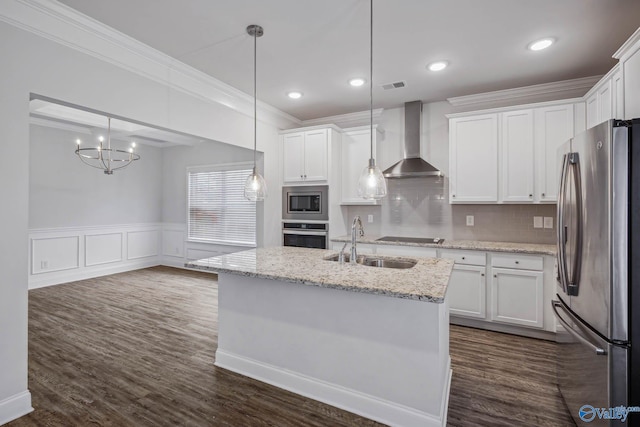 kitchen with pendant lighting, appliances with stainless steel finishes, white cabinetry, an island with sink, and wall chimney exhaust hood