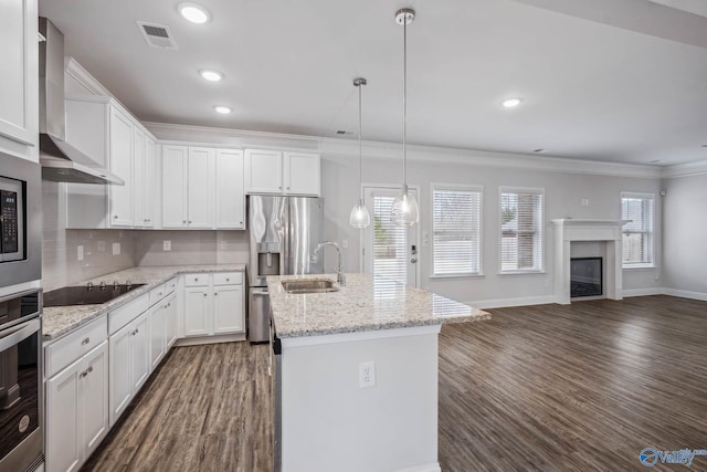 kitchen with stainless steel appliances, an island with sink, white cabinets, decorative light fixtures, and wall chimney exhaust hood