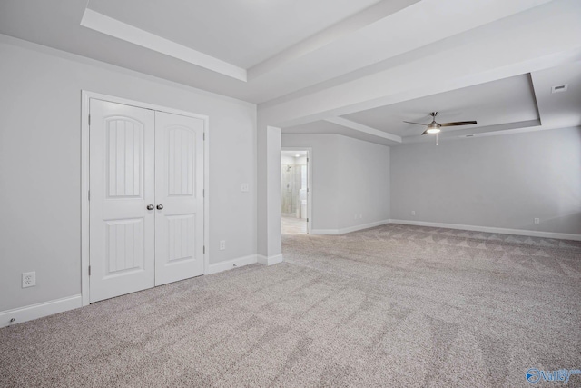 unfurnished bedroom with a tray ceiling, a closet, ceiling fan, and carpet