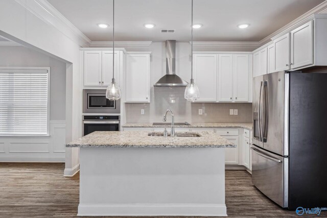 kitchen featuring stainless steel appliances, light stone countertops, an island with sink, decorative light fixtures, and wall chimney exhaust hood