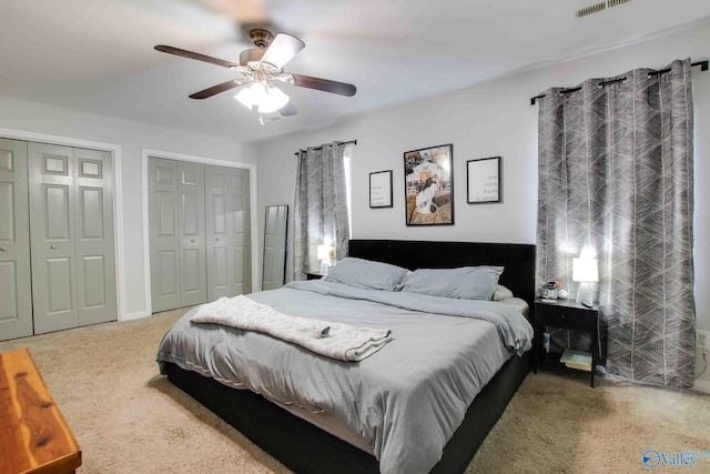 carpeted bedroom with ceiling fan and two closets