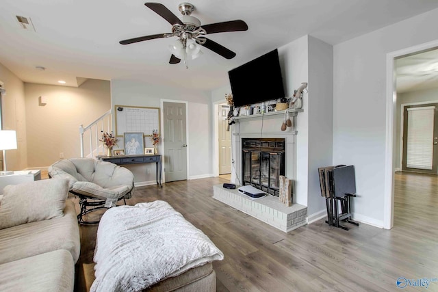 living room with hardwood / wood-style flooring, a brick fireplace, and ceiling fan