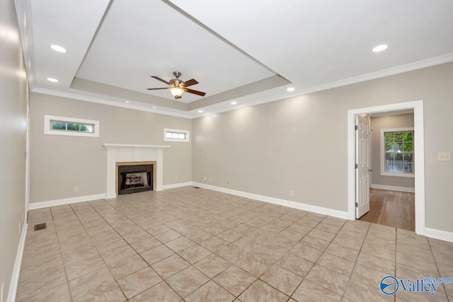 unfurnished living room with a tray ceiling, plenty of natural light, a fireplace, and a ceiling fan