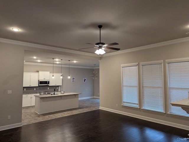 kitchen with crown molding, white cabinets, a center island with sink, and hanging light fixtures