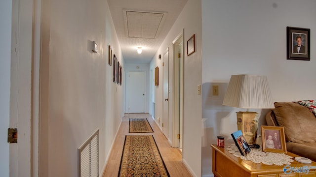 hall featuring light wood-style flooring, attic access, baseboards, and visible vents