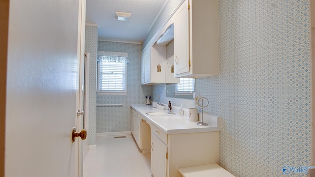 kitchen with white cabinets, a sink, ornamental molding, light countertops, and wallpapered walls