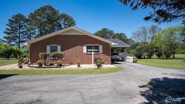 view of side of property with crawl space, an attached carport, aphalt driveway, brick siding, and a yard