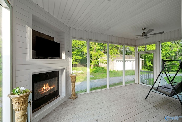 unfurnished sunroom featuring a ceiling fan and a glass covered fireplace