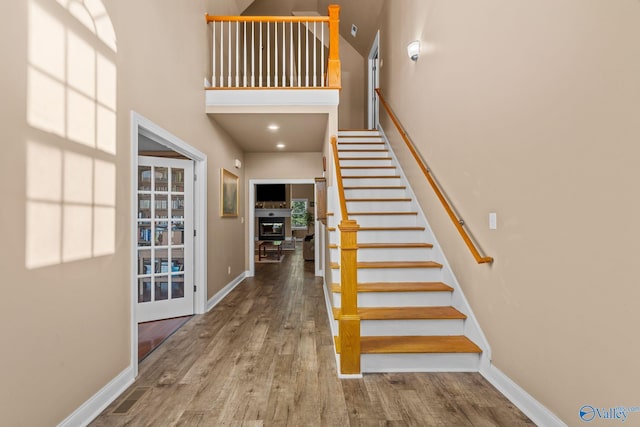 staircase featuring wood finished floors, baseboards, and a high ceiling