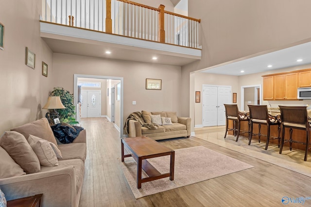 living room with recessed lighting, a high ceiling, baseboards, and light wood-type flooring