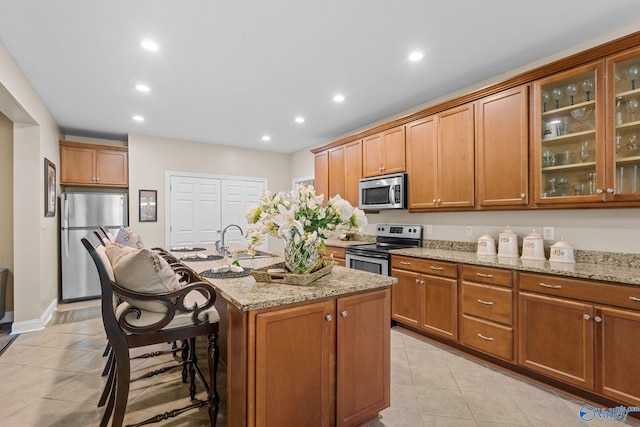 kitchen with a sink, a kitchen island with sink, light stone countertops, and stainless steel appliances