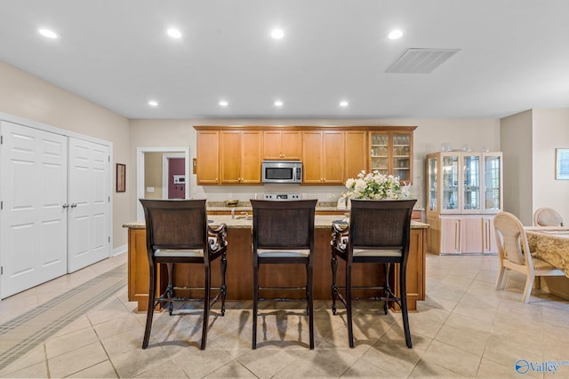 kitchen with a kitchen island with sink, recessed lighting, stainless steel microwave, visible vents, and glass insert cabinets