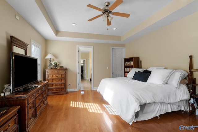 bedroom featuring baseboards, light wood-type flooring, recessed lighting, a raised ceiling, and a ceiling fan