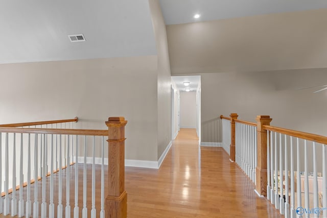 corridor with baseboards, visible vents, wood finished floors, and an upstairs landing