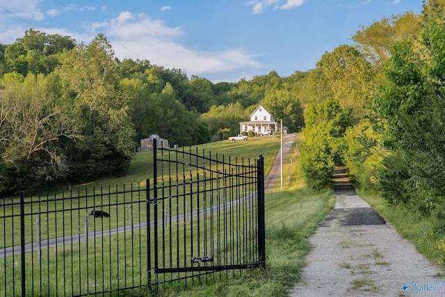 view of gate with a lawn, fence, a rural view, and a forest view
