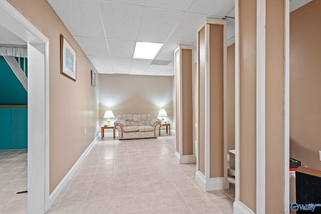 hallway with light tile patterned floors, baseboards, and a paneled ceiling