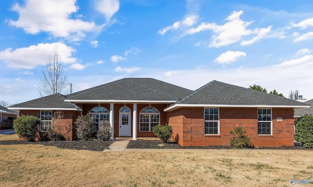 single story home with a shingled roof, a front lawn, and brick siding