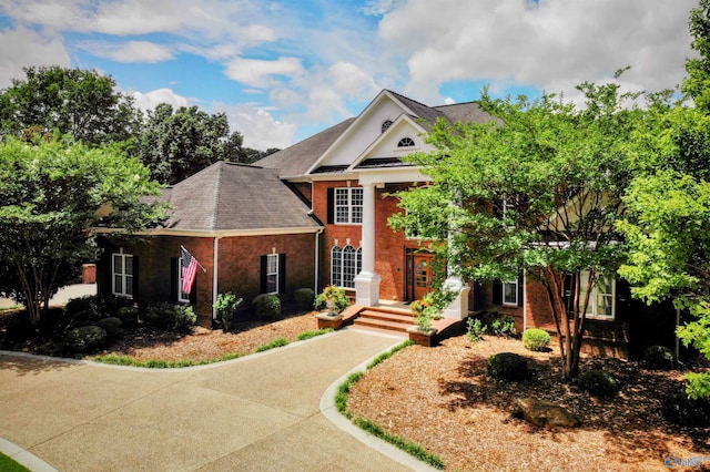 neoclassical home featuring a shingled roof and brick siding