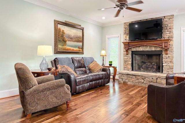 living area featuring a stone fireplace, wood finished floors, crown molding, baseboards, and ceiling fan