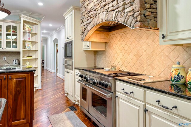 kitchen with dark stone counters, double oven range, backsplash, crown molding, and dark wood-type flooring