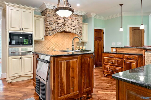 kitchen with black microwave, light hardwood / wood-style floors, hanging light fixtures, decorative backsplash, and sink