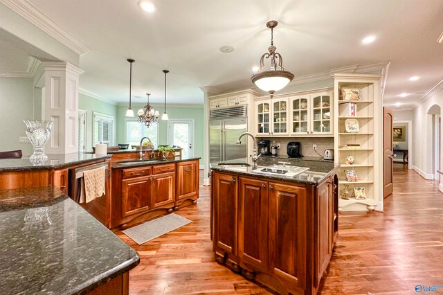 kitchen with appliances with stainless steel finishes, sink, light wood-type flooring, dark stone countertops, and a spacious island