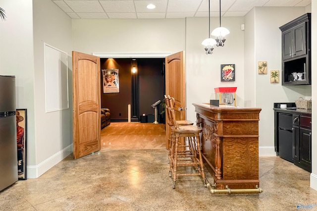 interior space featuring decorative light fixtures, baseboards, a drop ceiling, and freestanding refrigerator