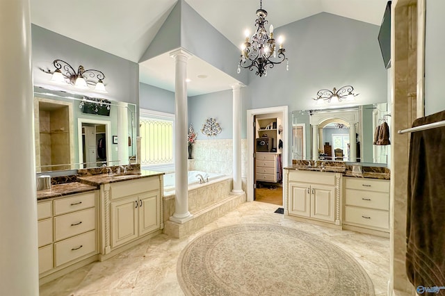 full bathroom with two vanities, a sink, ornate columns, a garden tub, and high vaulted ceiling
