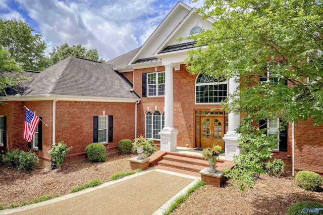 greek revival inspired property with a shingled roof, french doors, and brick siding