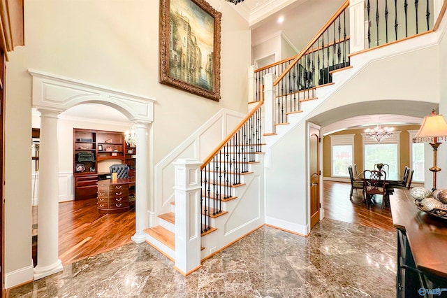 stairs with hardwood / wood-style flooring, crown molding, decorative columns, and an inviting chandelier