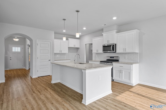 kitchen featuring arched walkways, white cabinets, an island with sink, appliances with stainless steel finishes, and a sink