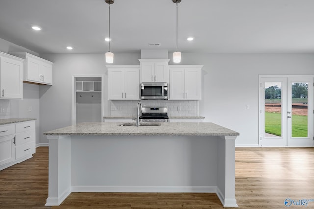 kitchen with light stone counters, appliances with stainless steel finishes, white cabinetry, pendant lighting, and a sink